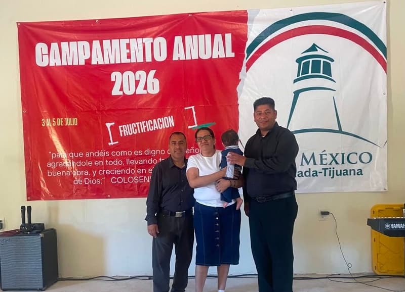 A family standing in front of the 2026 annual camp banner with the IPUL Mexico logo.