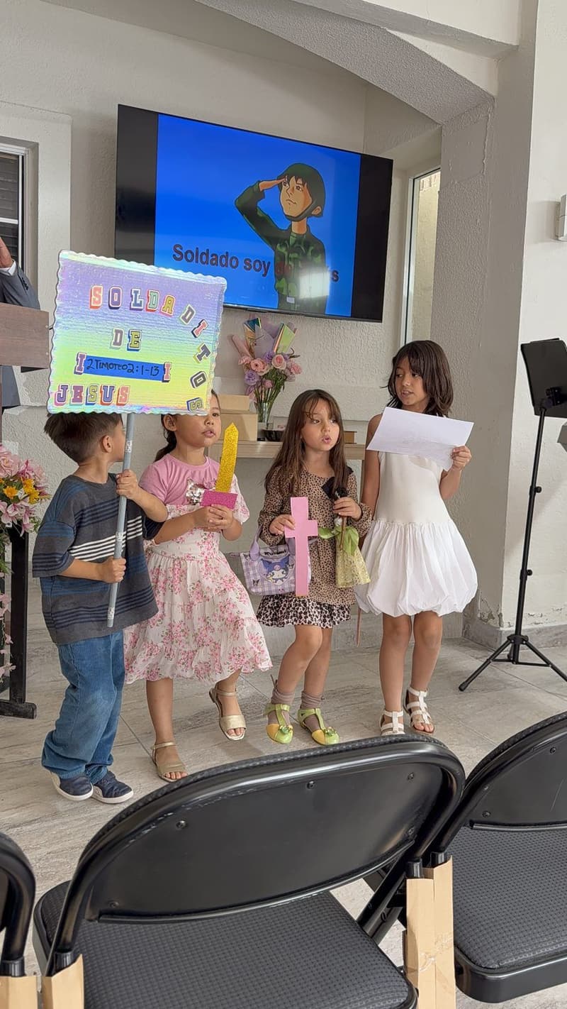 Four children at the front of the church holding paper swords and a sign that reads "Soldado de Jesús", with a song slide on the screen behind them.
