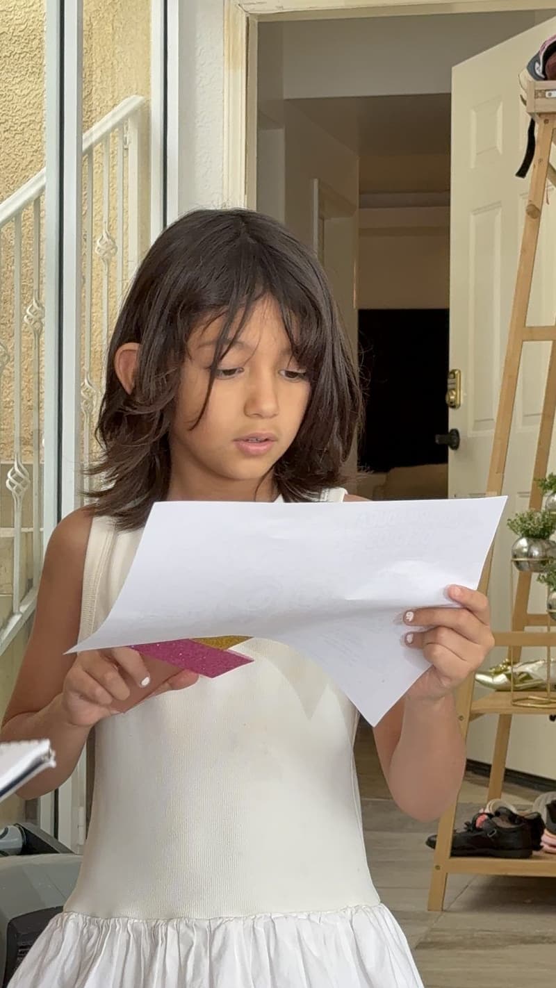 A girl in a white dress reading from a sheet of paper.