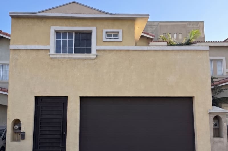 IPUL Tijuana from the street: a two-story yellow house with a dark iron gate and a garage door.